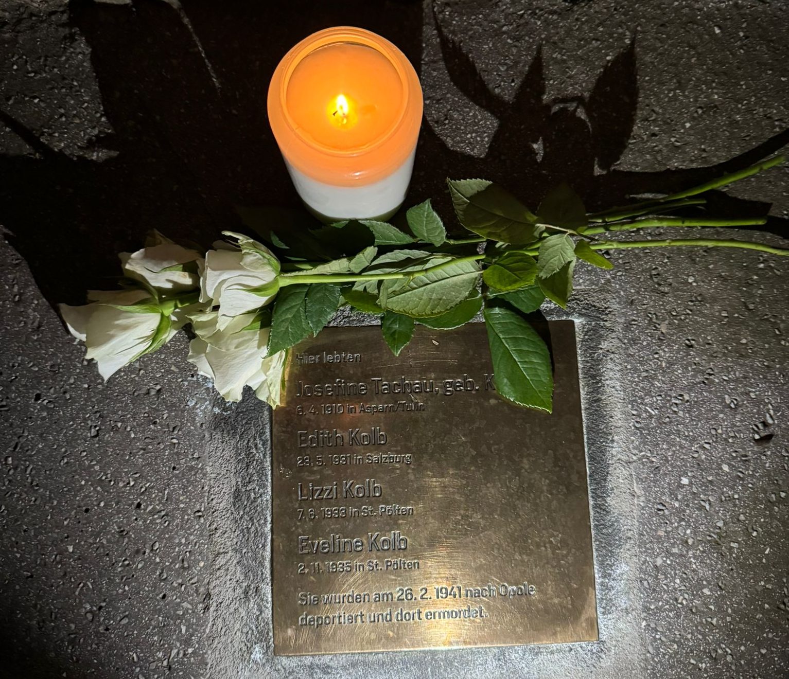 Ein Foto des Steins auf dem die Namen der Familie eingraviert sind, mit einer Kerze beleuchtet.