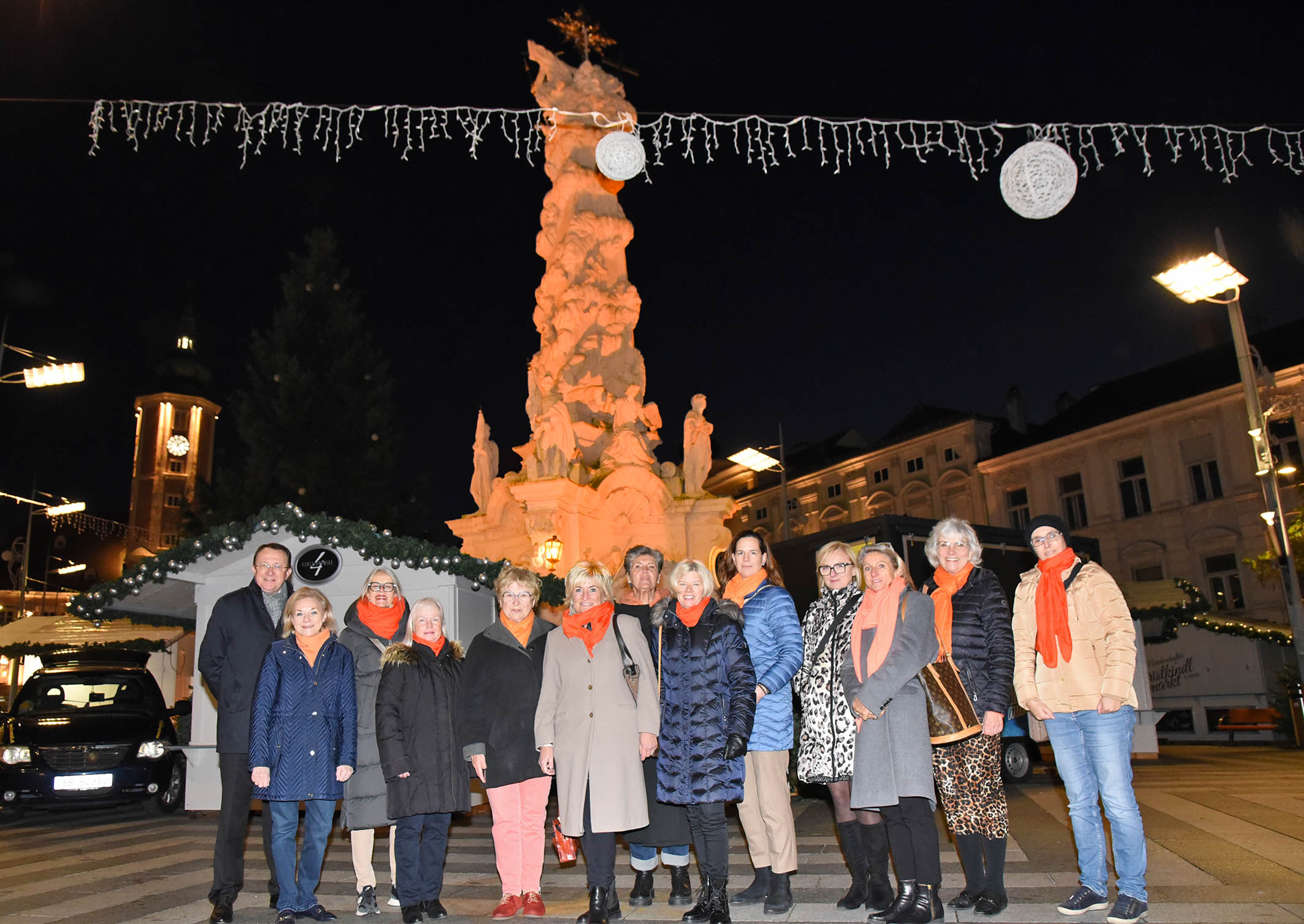 Soroptimistinnen stehen mit Bürgermeister Stadler vor dem orange beleuchteten Brunnen am Rathausplatz. Foto: Josef Vorlaufer.